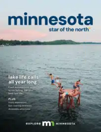 Minnesota Vacation Guide: A scenic view of a lighthouse on a rocky cliff overlooking a vast blue lake during a clear day in Minnesota.