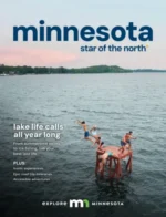 Minnesota Vacation Guide: A scenic view of a lighthouse on a rocky cliff overlooking a vast blue lake during a clear day in Minnesota.