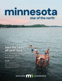 Minnesota Vacation Guide: A scenic view of a lighthouse on a rocky cliff overlooking a vast blue lake during a clear day in Minnesota.