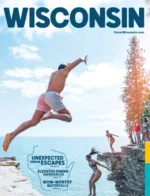Wisconsin Vacation Guide: A scenic view of the Wisconsin shoreline featuring clear blue water and lush green trees under a bright sky.