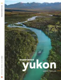 A scenic view of the Yukon River winding through a valley of autumnal boreal forest under a clear blue sky.